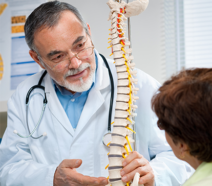 Older physician with beard shows a model of the spine to young physicians patient