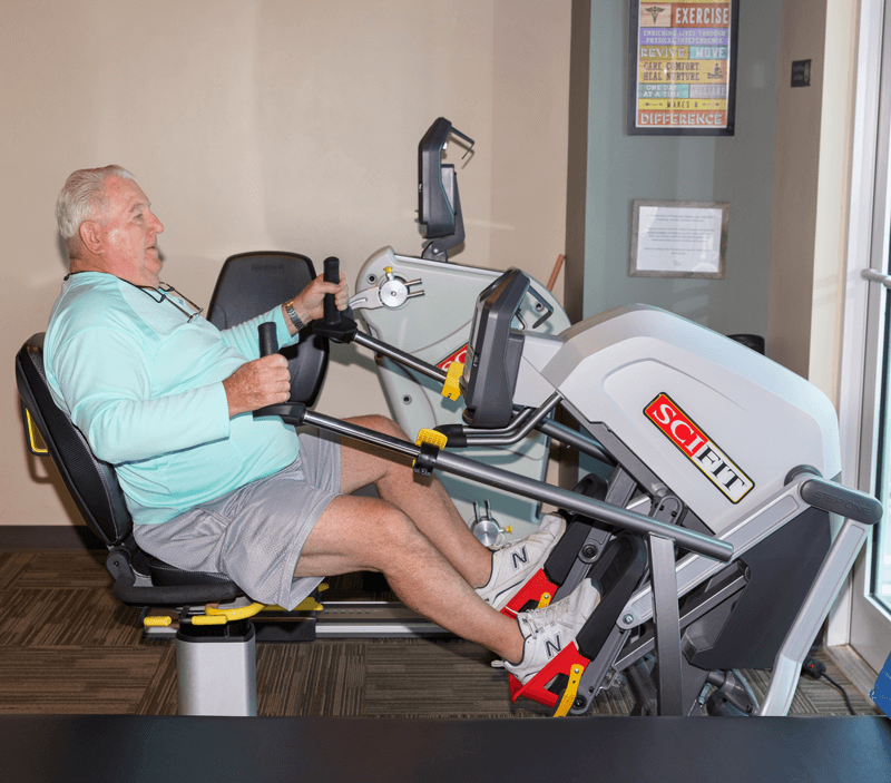 Senior patient riding physical therapy bicycle at office gym